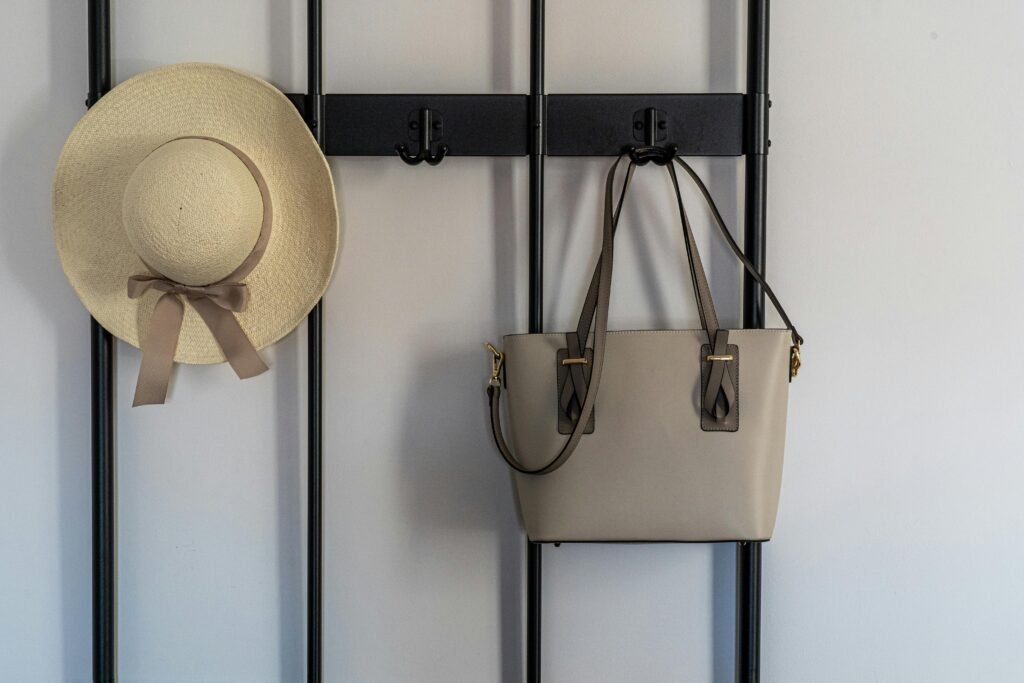 A stylish sun hat and leather handbag hanging on a modern wall hook indoors.